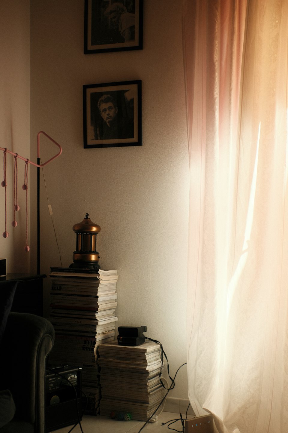 An armchair and stacks of magazines sit near a window.